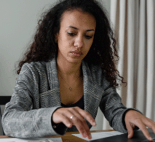 A woman at her desk in front of a laptop doing calculations on a desk calculator