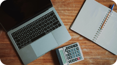 A desktop view with a laptop on it, a calculator, and a notebook.