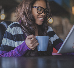 A woman holding a coffee mug and looking at her tablet device